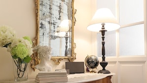 A wooden console table with a mirror, a lamp, a globe, and a vase with flowers.
