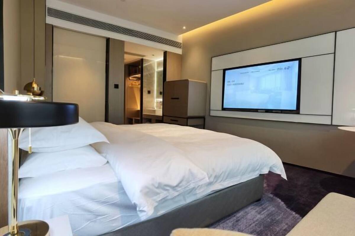 Ein modernes Hotelzimmer mit einem großen Bett, einem an der Wand befestigten Fernseher und einem begehbaren Kleiderschrank.