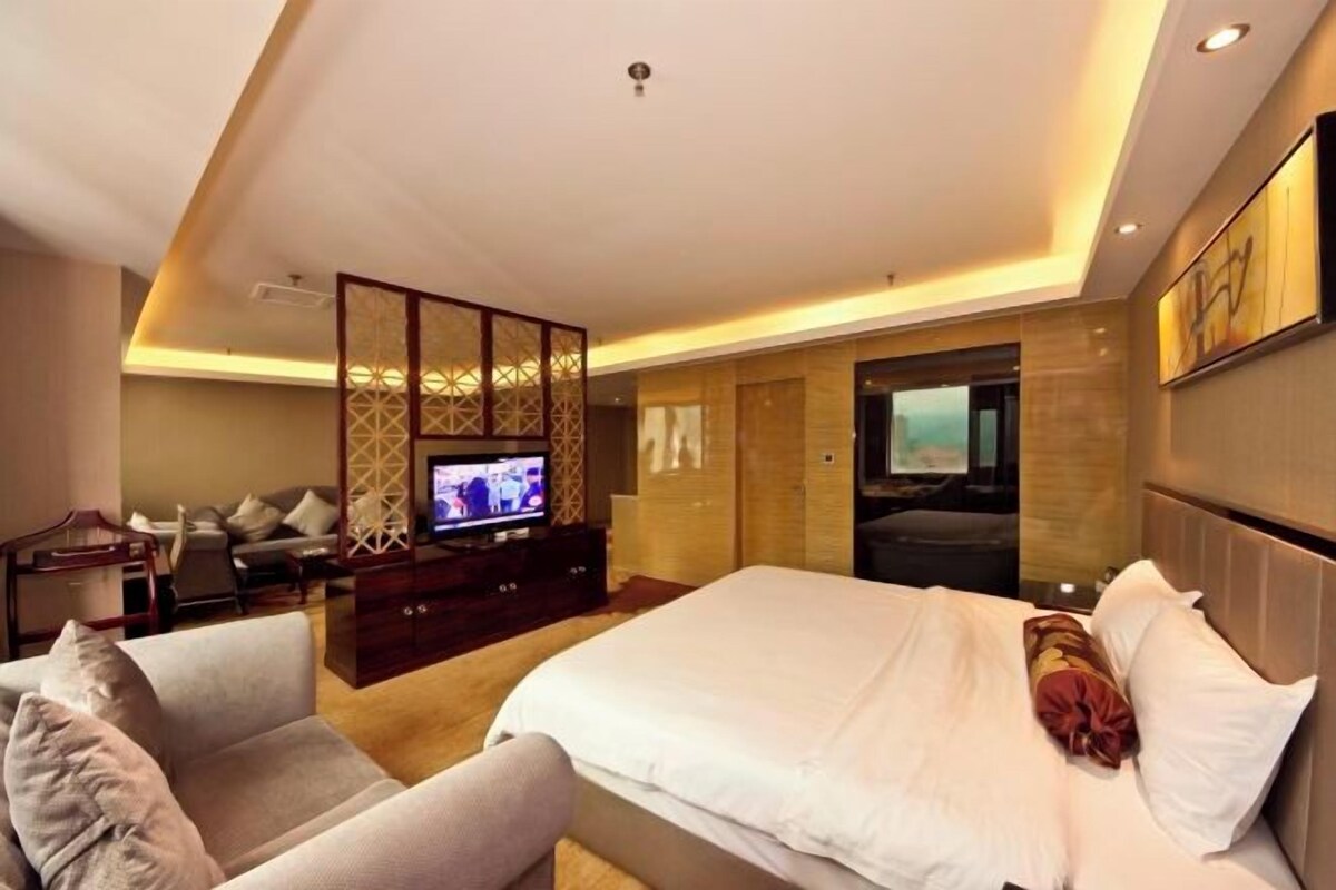 A modern hotel room with a large bed, a TV, a seating area with a sofa and armchairs, and a decorative screen.