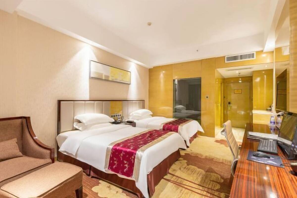 Ein Hotelzimmer mit zwei Betten, einem Schreibtisch mit Computer, einem Sessel und einem großen Spiegel an der Wand.