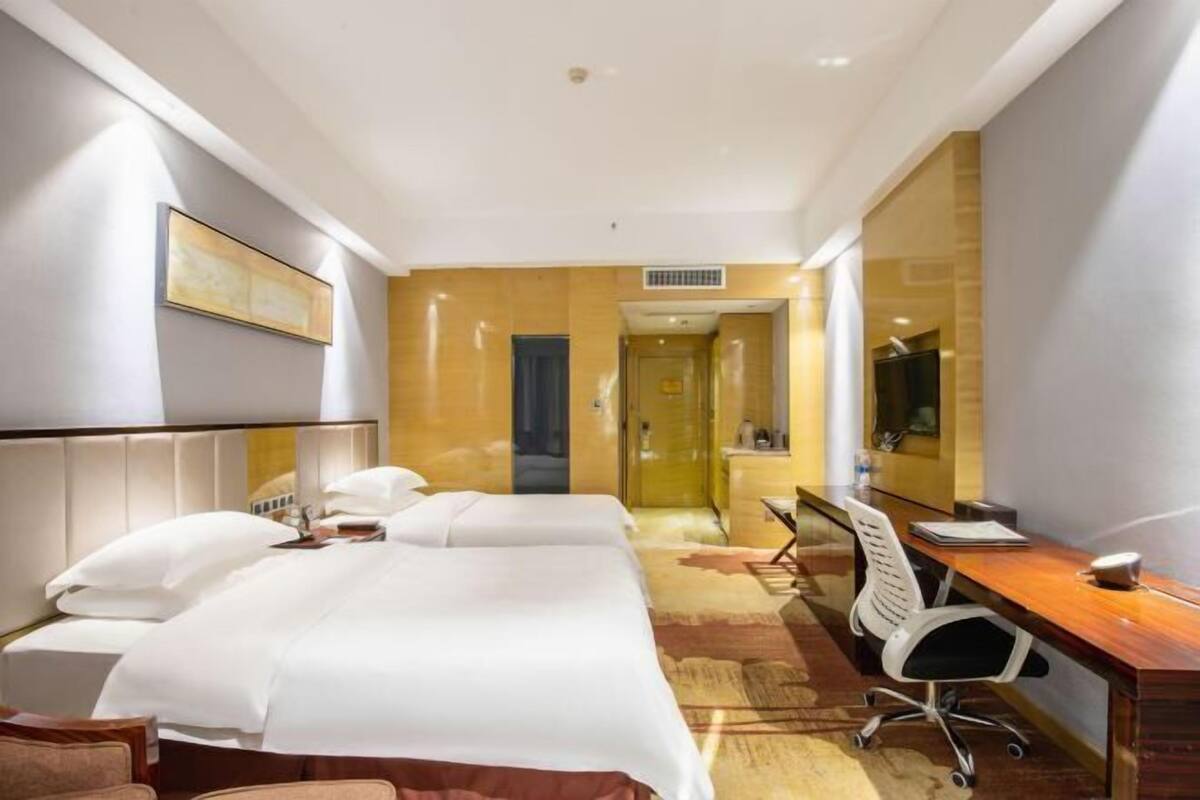 Ein Hotelzimmer mit zwei Betten, einem Schreibtisch, einem Stuhl und einem Spiegel.