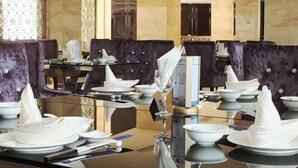 Un ambiente de restaurante con mesas dispuestas para comer, destacando sillas tapizadas en color púrpura y vajilla blanca.