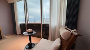 Habitación de hotel con una cama, una mesita con una taza y un plato, y vistas de la ciudad a través de amplias ventanas.