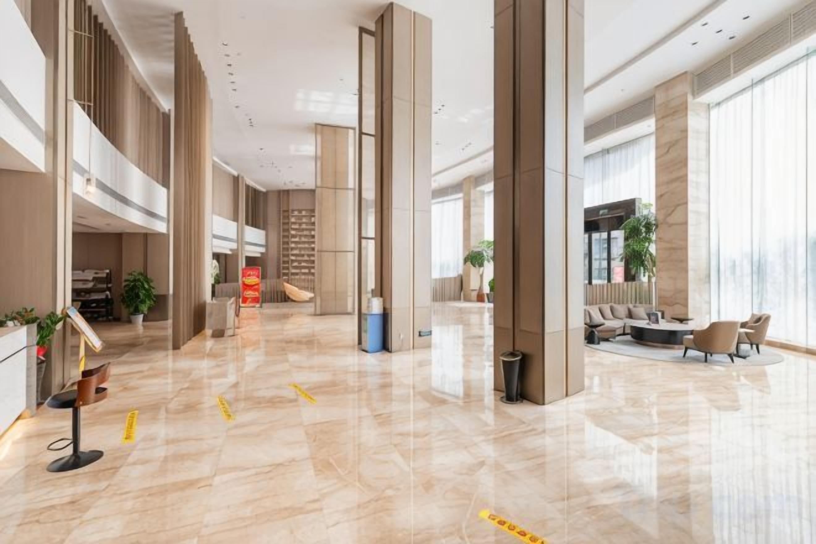 Un vestíbulo amplio con techo alto, una recepción, zona de estar y ventanas grandes.