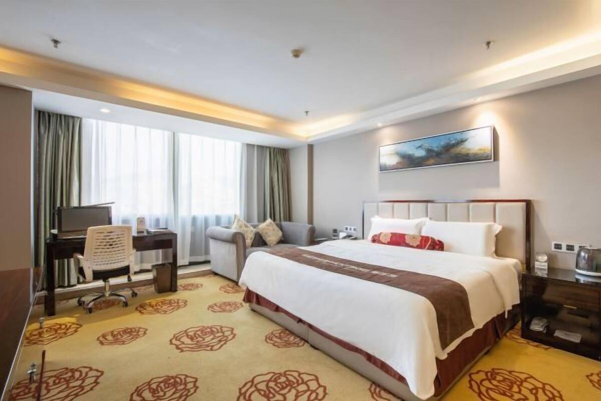 Ein Hotelzimmer mit einem großen Bett, einem Schreibtisch mit Stuhl, einem Fernseher und einem Bild an der Wand.