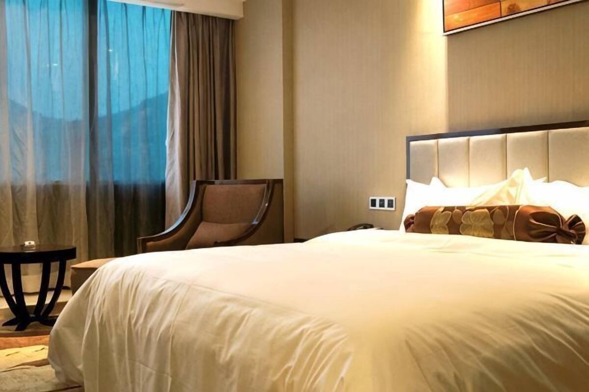 Ein Hotelzimmer mit einem großen Bett, einem Sessel, einem kleinen Tisch und Blick durch ein Fenster mit Vorhängen.