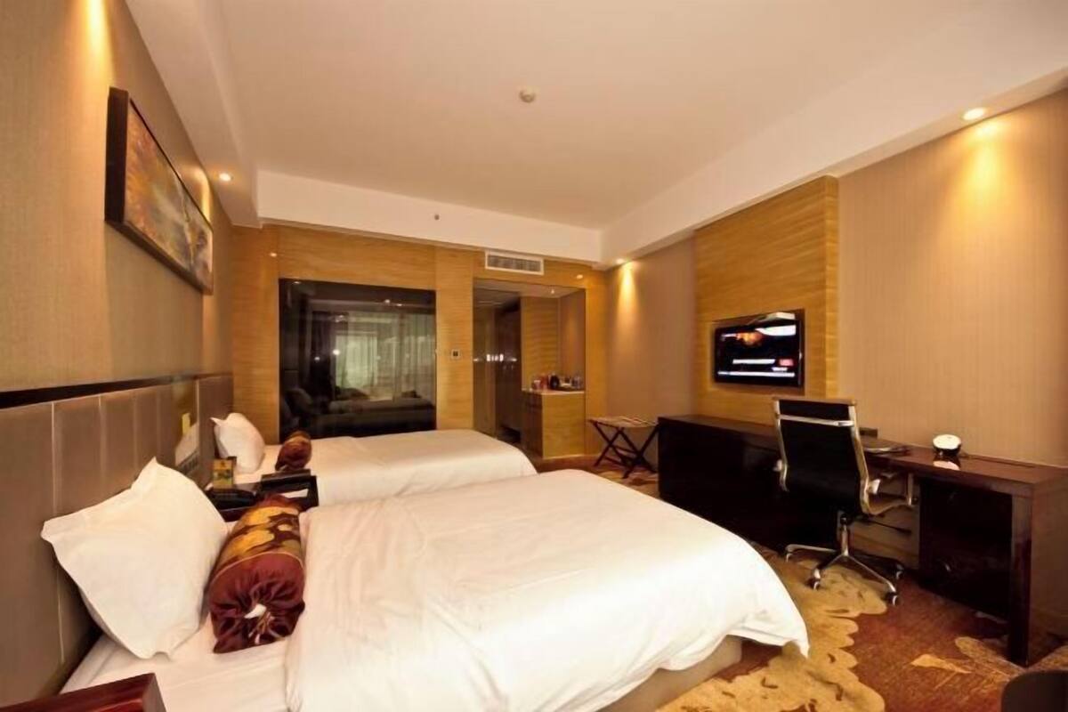 Ein Hotelzimmer mit zwei Betten, einem Fernseher, einem Schreibtisch und einem Stuhl.