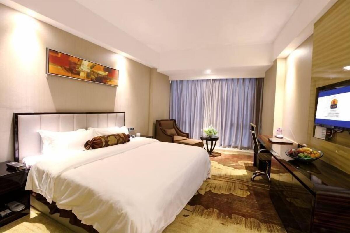 Ein Hotelzimmer mit Bett, Schreibtisch, Stuhl, Fernseher und einem Fenster mit Vorhängen.