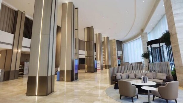 Un vestíbulo amplio con columnas altas y elegantes, una zona de estar con sofás y sillones, y un gran ventanal que proporciona luz natural.