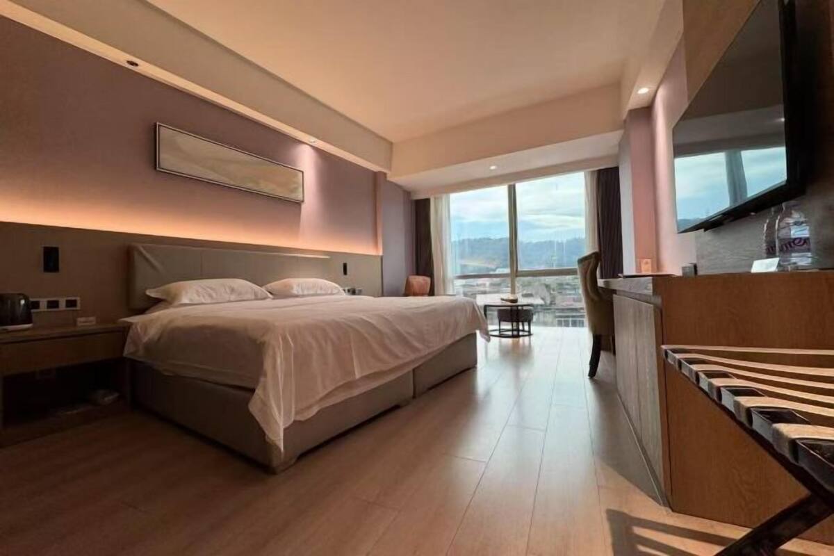 Ein modernes Hotelzimmer mit einem großen Bett, einem Schreibtisch, einem Fernseher und Blick auf die Stadt.