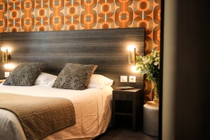 A neatly made bed with two pillows, a bedside table with a book, and a wall with a geometric pattern. - Hôtel Le G (Nice)