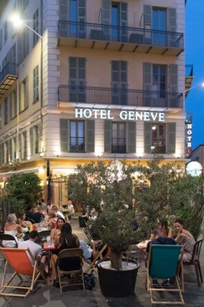 Exterior de un hotel con asientos al aire libre y un gran árbol en maceta.
