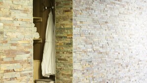 A bathroom with a stone wall and a wooden door. There is a towel hanging on a rack. - Hotel De Naaldhof (Oss)