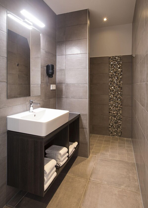 A modern bathroom with a large sink, dark wood vanity, and a shower with a mosaic tile wall.