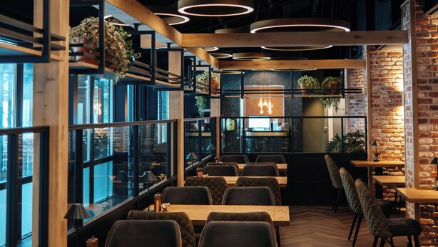 A modern restaurant interior with wooden tables, cushioned chairs, and circular ceiling lights. - Hotel De Naaldhof (Oss)