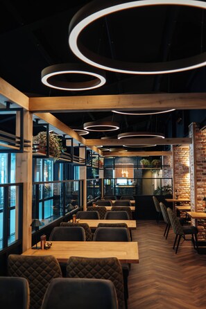 A modern restaurant interior with wooden tables, cushioned chairs, and circular ceiling lights.