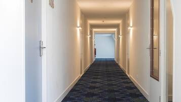 Un corridoio di un hotel con pavimenti rivestiti di moquette, porte su entrambi i lati e un segnale di uscita verde sul soffitto.