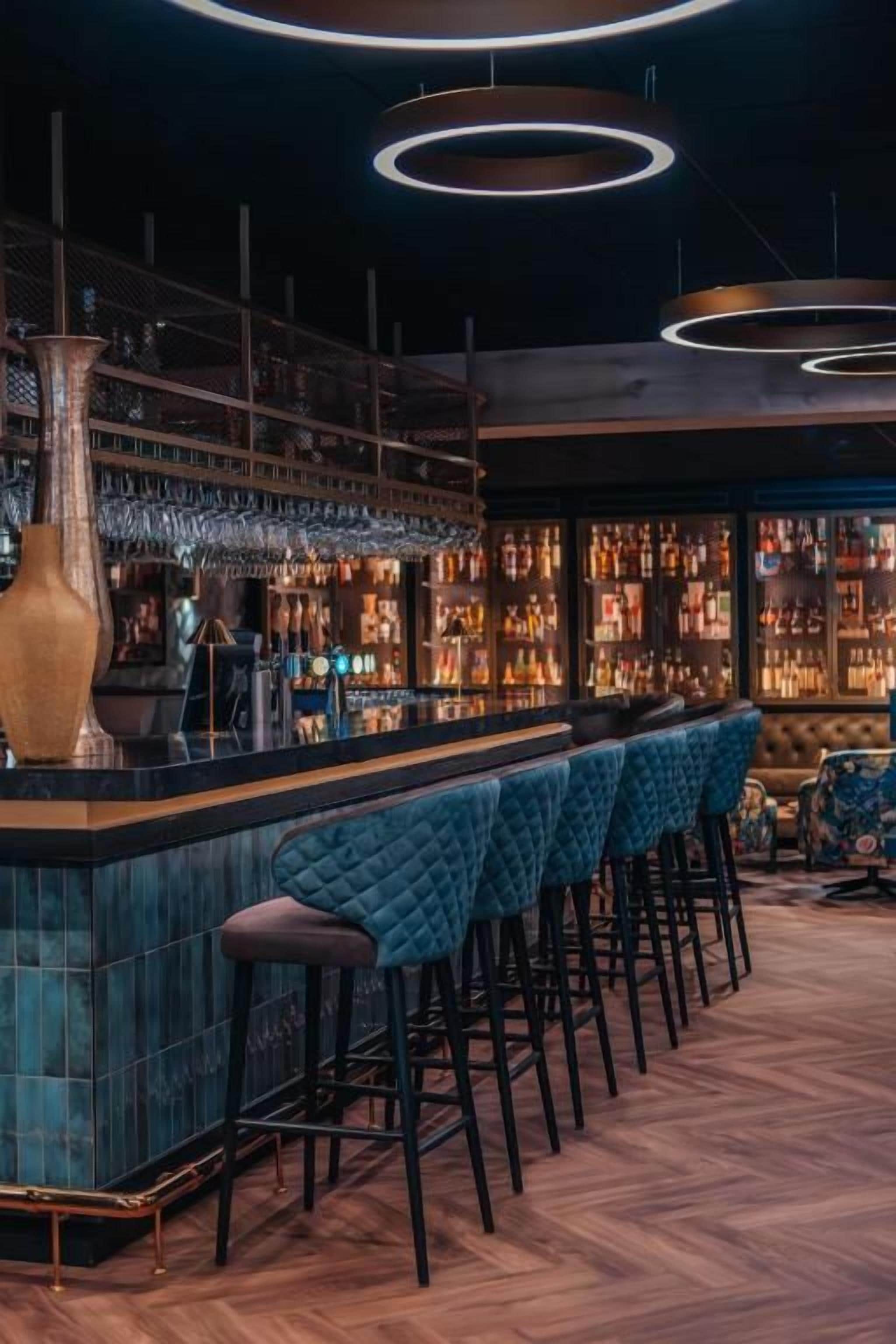 A bar area with a long counter, multiple stools, and a variety of bottles and glasses.