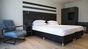 A modern bedroom with a bed, a chair, a nightstand, and a wardrobe. - Hotel De Naaldhof (Oss)