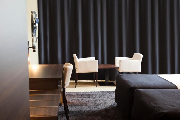 A hotel room with a bed, two white chairs, a wooden desk, and a black curtain. - Hotel De Naaldhof (Oss)