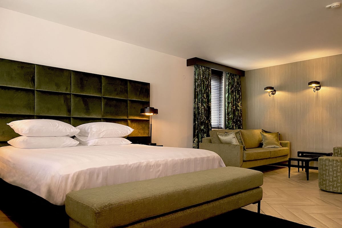 Ein modernes Hotelzimmer mit einem großen Bett, einer Couch, einer Bank und einem kleinen Tisch.