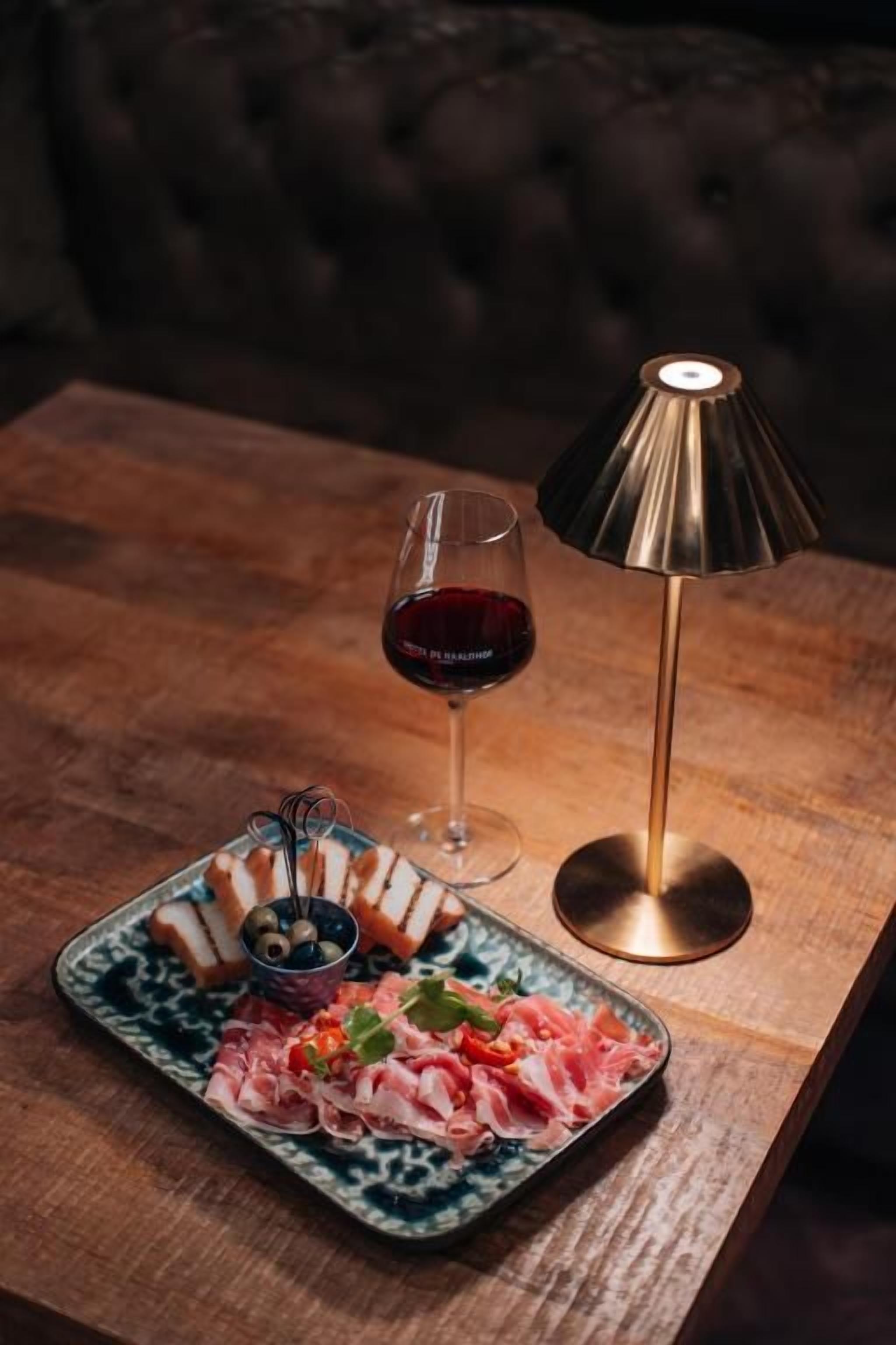 Ein Tisch mit Essen, einem Weinglas und einer Lampe.