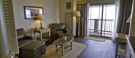 Amplia sala de estar con sofá, sillón y mesa de centro, un balcón con cortinas y vistas al exterior.
