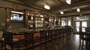 A bar area with a long counter, multiple bar stools, and a television screen mounted on the wall.
