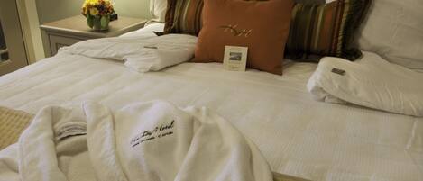 Una cama bien hecha con sábanas blancas, una almohada marrón con un logotipo y una bata blanca sobre la cama.
