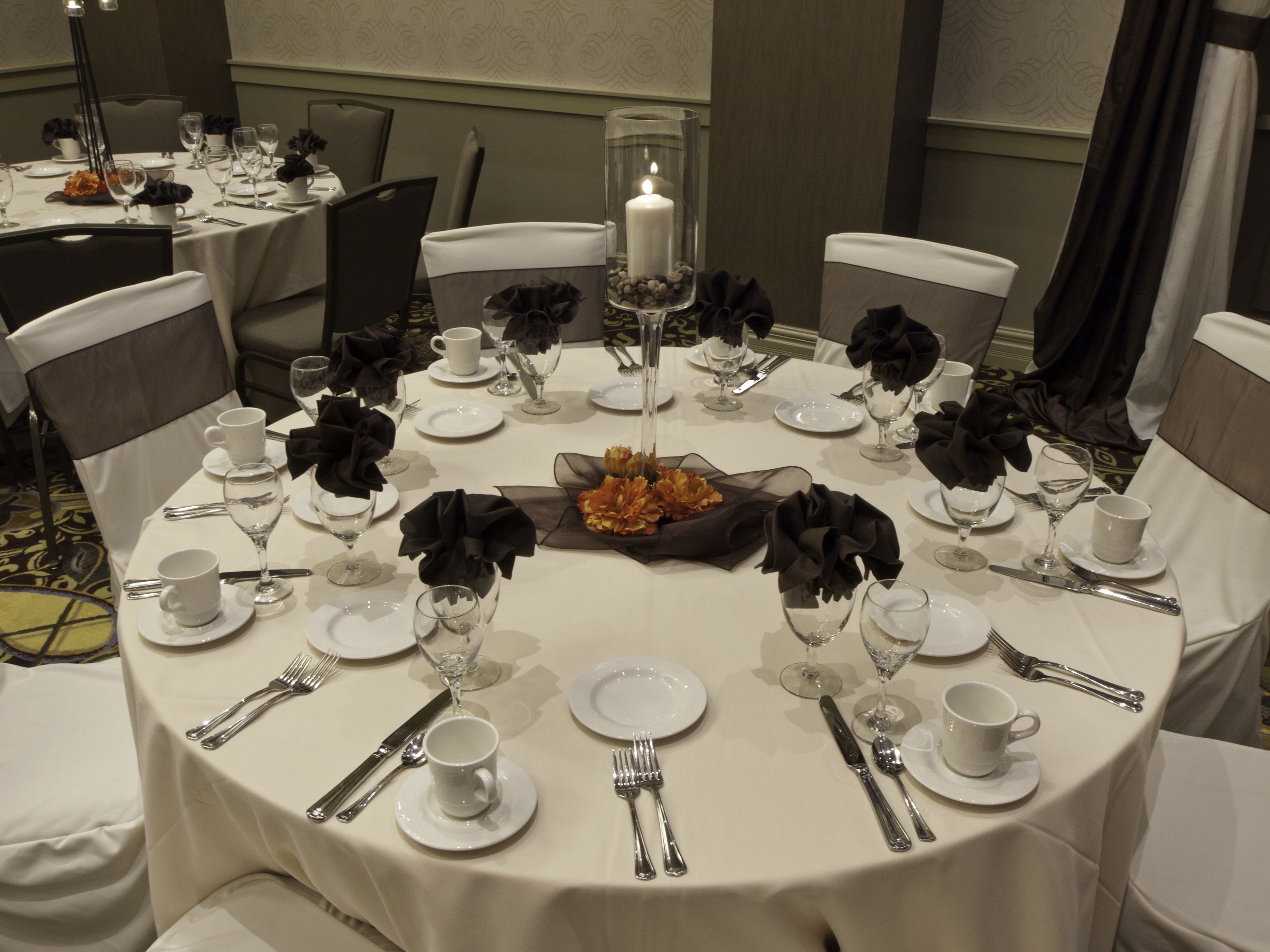 A round dining table set for a formal meal with white tablecloths, black napkins, and clear glassware.