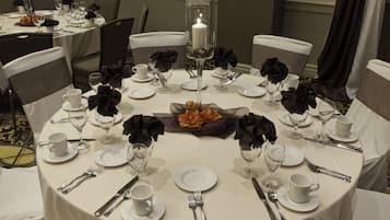 Une table ronde dressée pour un repas formel, avec une nappe blanche, des serviettes noires et de la vaisselle transparente.