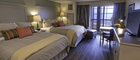A hotel room with two beds, a desk, a chair, a TV, and a view of the sea.