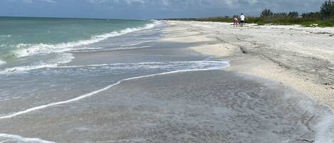 Di pantai, pasir putih, payung pantai, dan handuk pantai