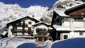 Un edificio de estilo chalé tradicional con fachada de madera y exterior blanco, rodeado de montañas cubiertas de nieve.