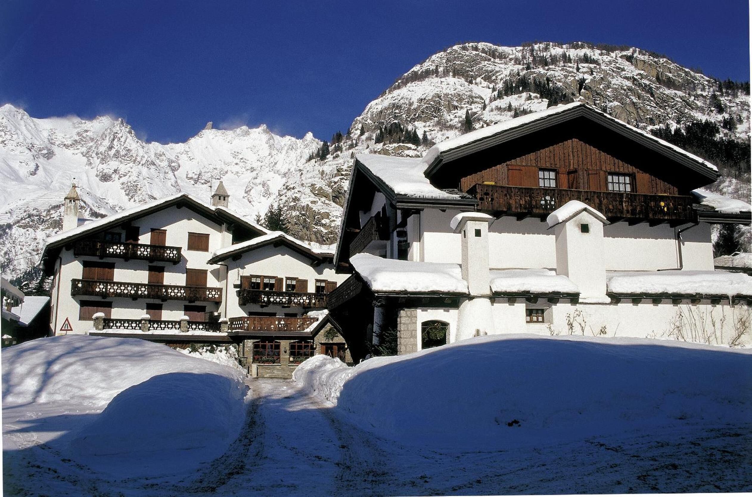 Un refugio de montaña cubierto de nieve con arquitectura alpina tradicional, que presenta balcones de madera y un techo empinado.