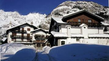 Un refugio de montaña cubierto de nieve con arquitectura alpina tradicional, que presenta balcones de madera y un techo empinado.