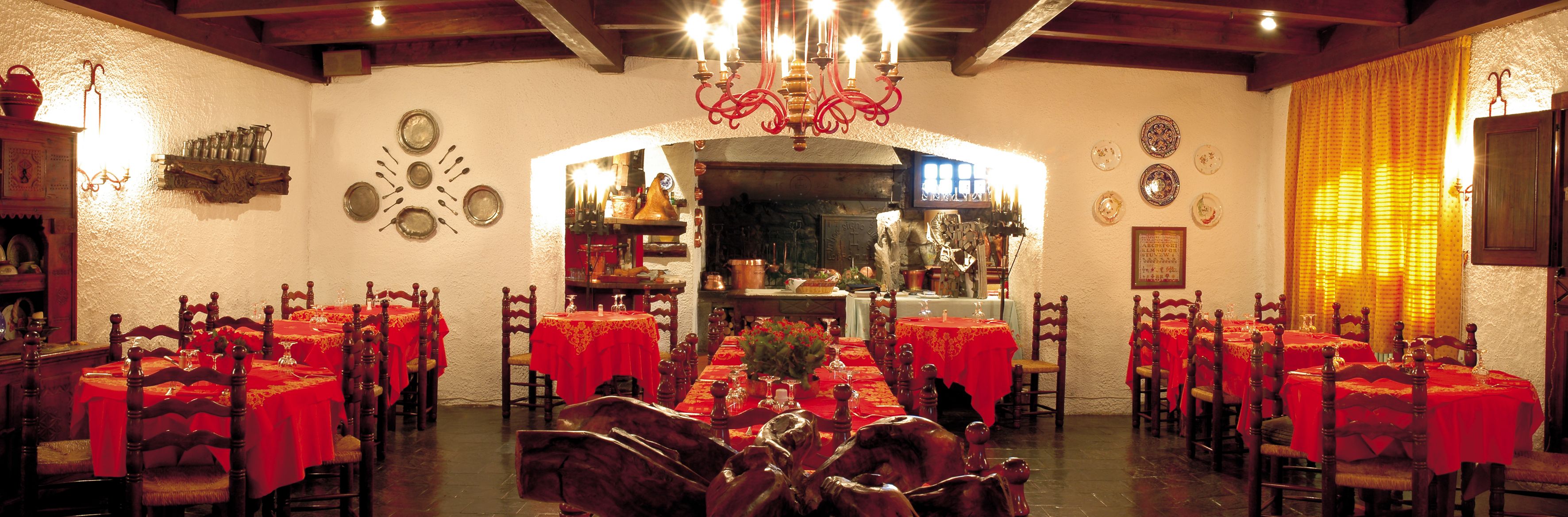 A dining area with multiple tables set for service, wooden chairs, and a chandelier.