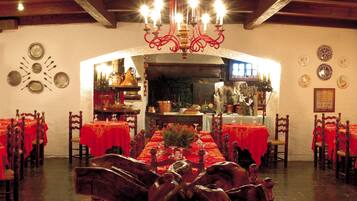A dining area with multiple tables set for service, wooden chairs, and a chandelier.