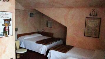 A small, dimly lit room with two single beds, a small table, and a chair.