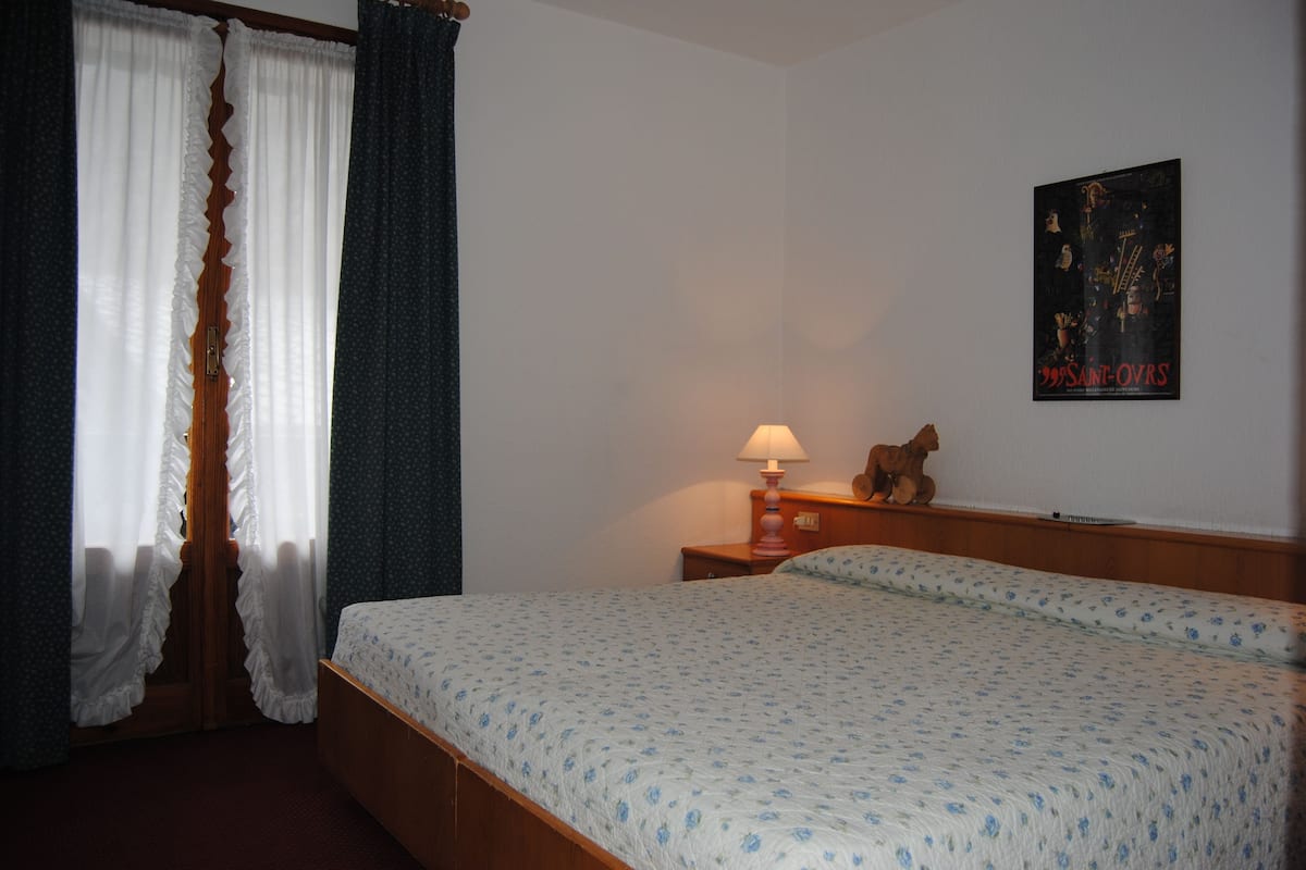 A bedroom with a bed, a nightstand with a lamp, a teddy bear, and a poster on the wall.