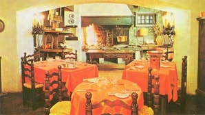 Un comedor con mesas dispuestas para cuatro, una chimenea y utensilios de cocina a la vista.