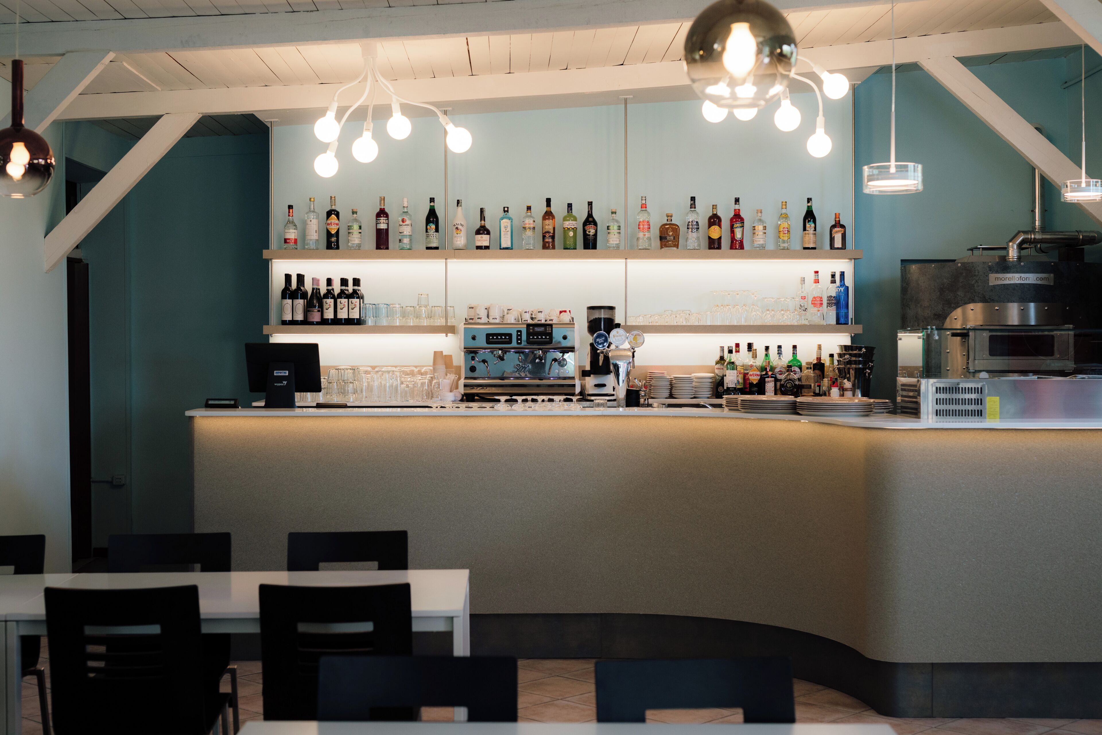 A bar area with a counter, shelves of bottles, glasses, and a coffee machine.