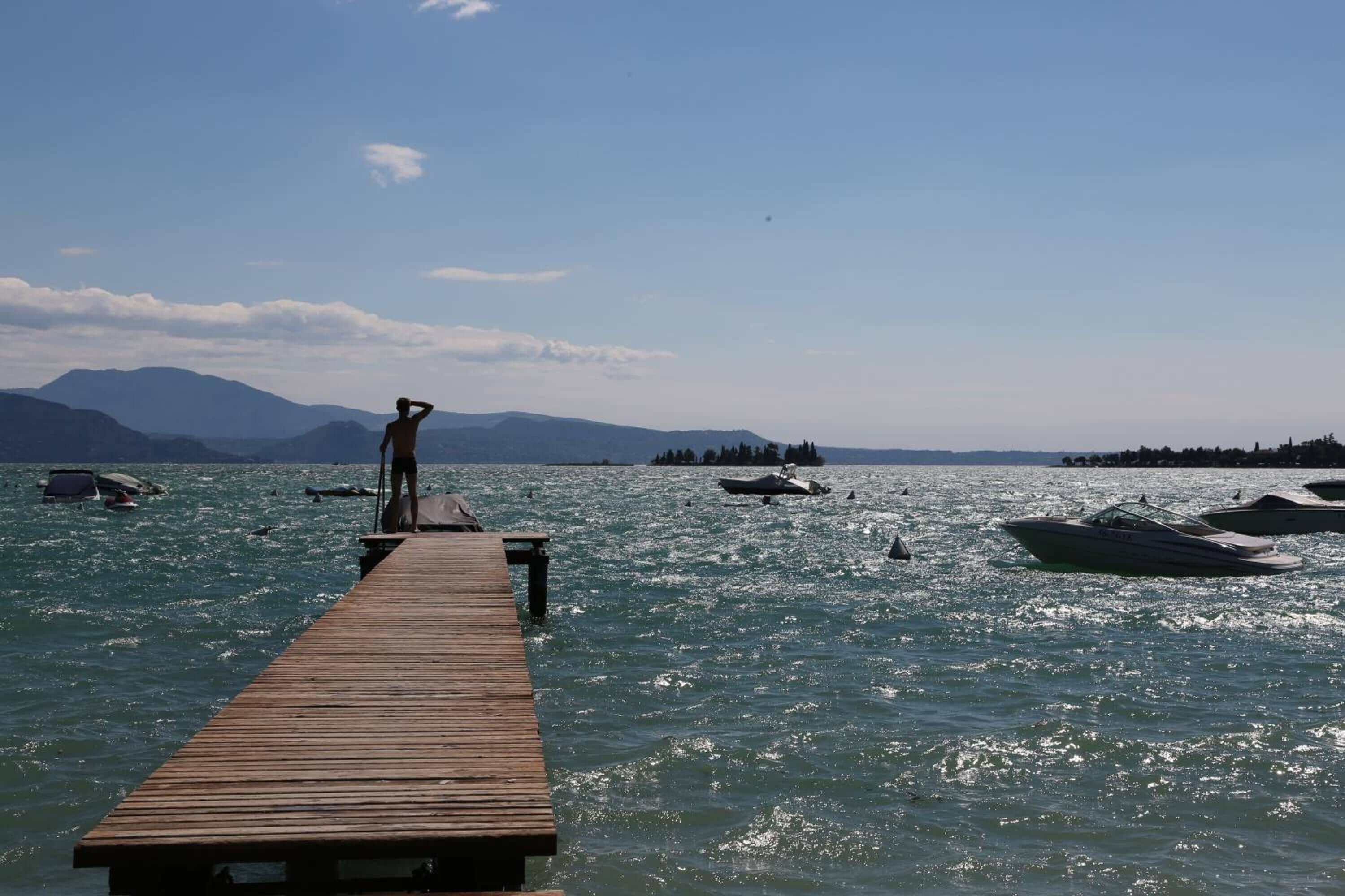 A wooden pier extending into a body of water with boats and a person standing at the end.