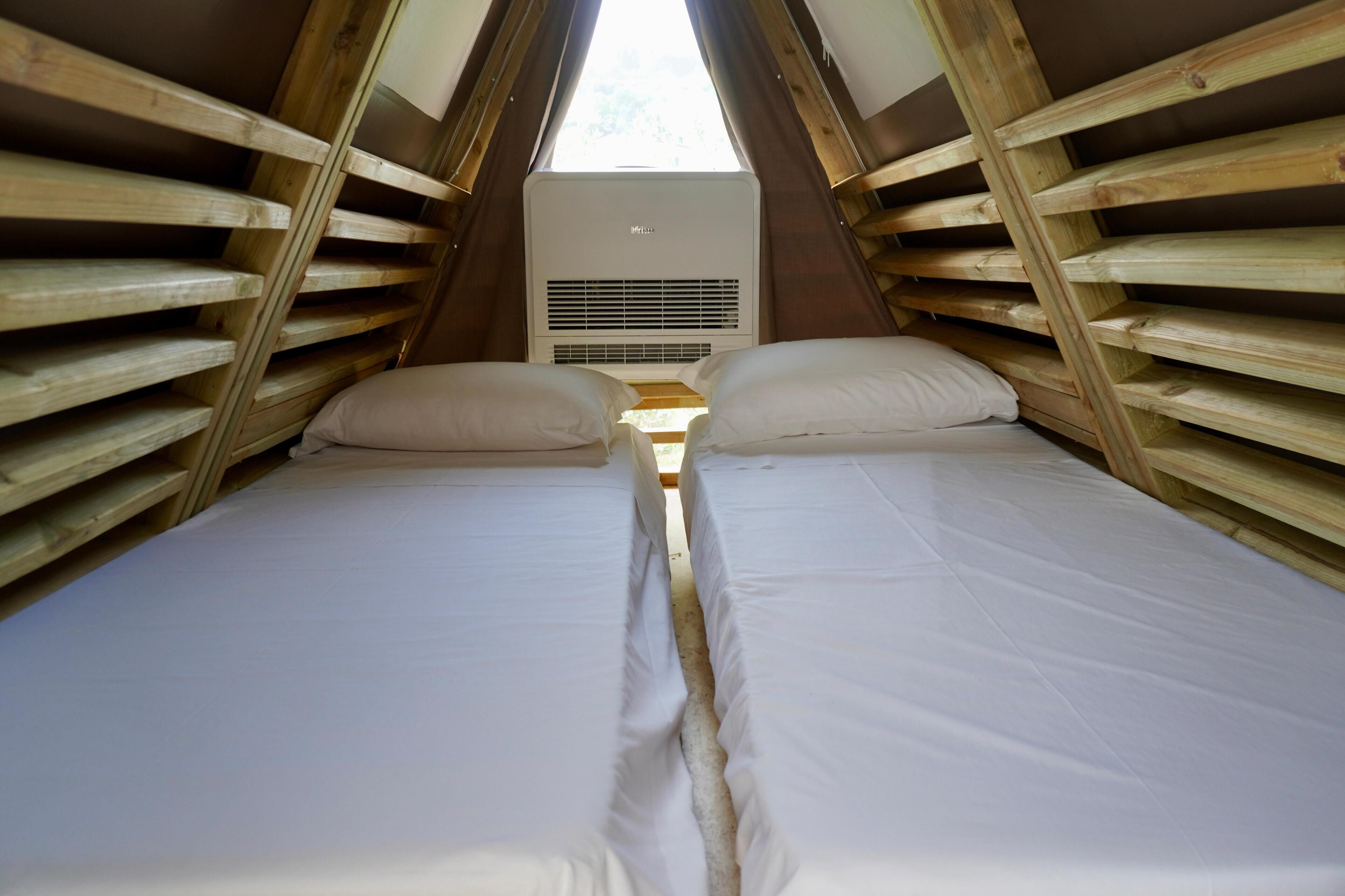 A small, cozy attic bedroom with two beds, wooden slats on the walls, and a skylight.