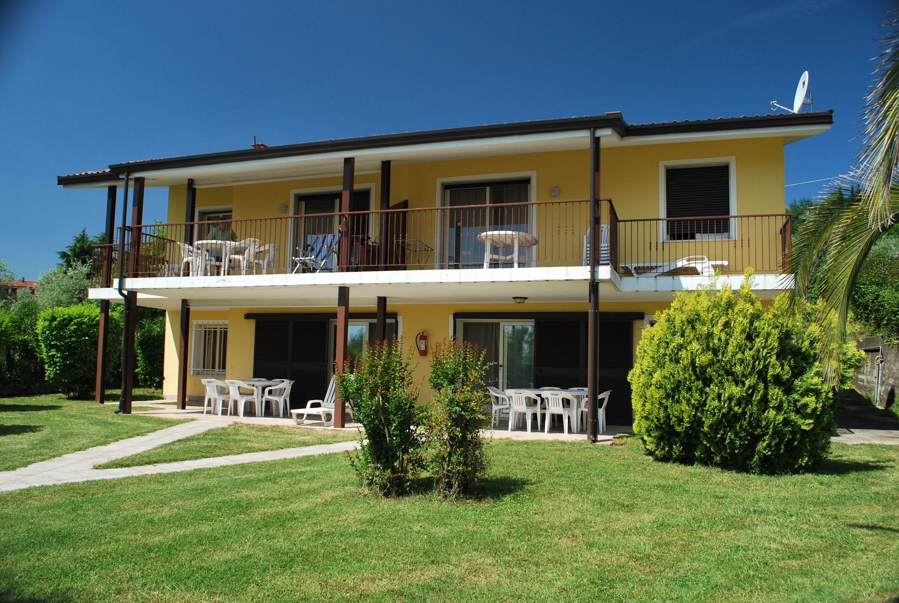 A two-story building with a balcony, outdoor seating, and a well-maintained lawn.