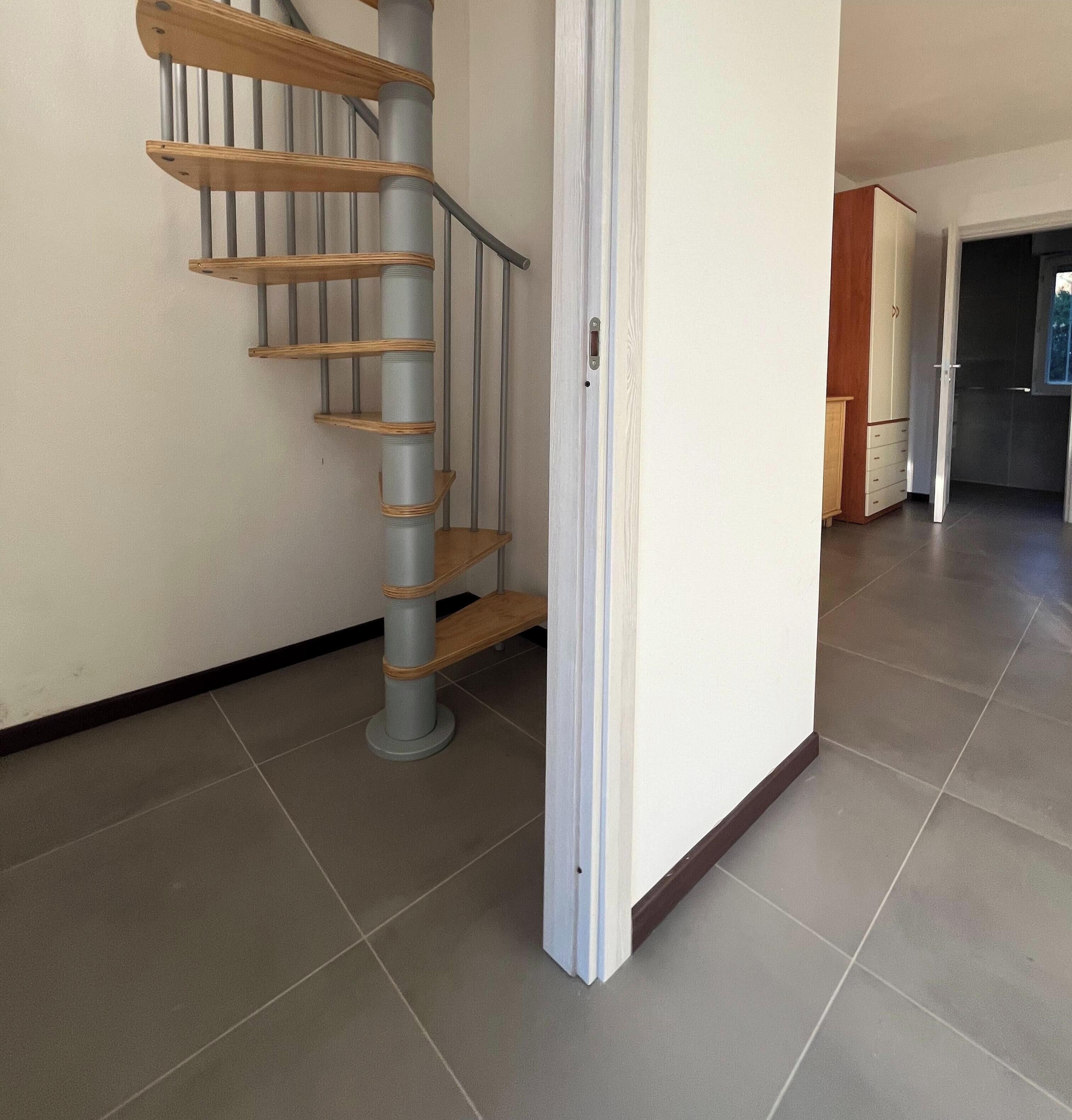Una escalera con escalones de madera y barandillas de metal, que conduce a una habitación con una puerta blanca y piso de baldosas.