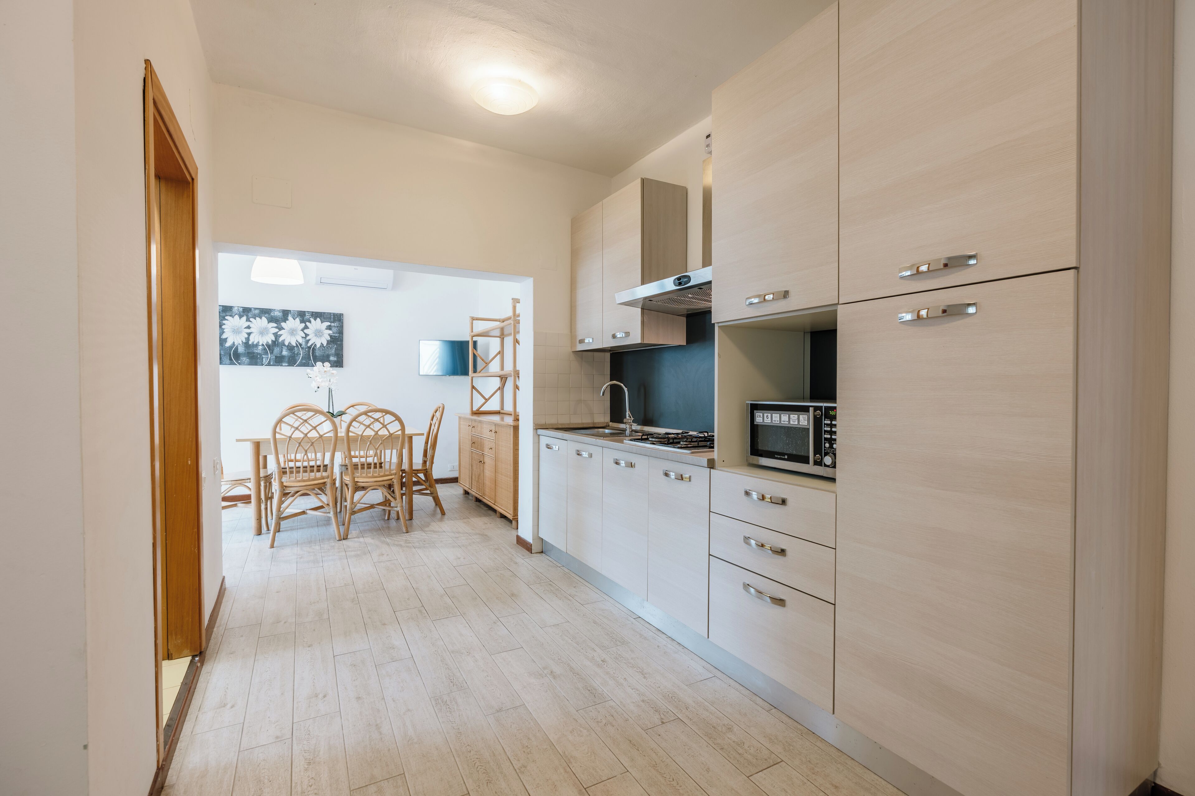 A modern kitchen with light wood cabinets, a microwave, and a dining area with a table and chairs.