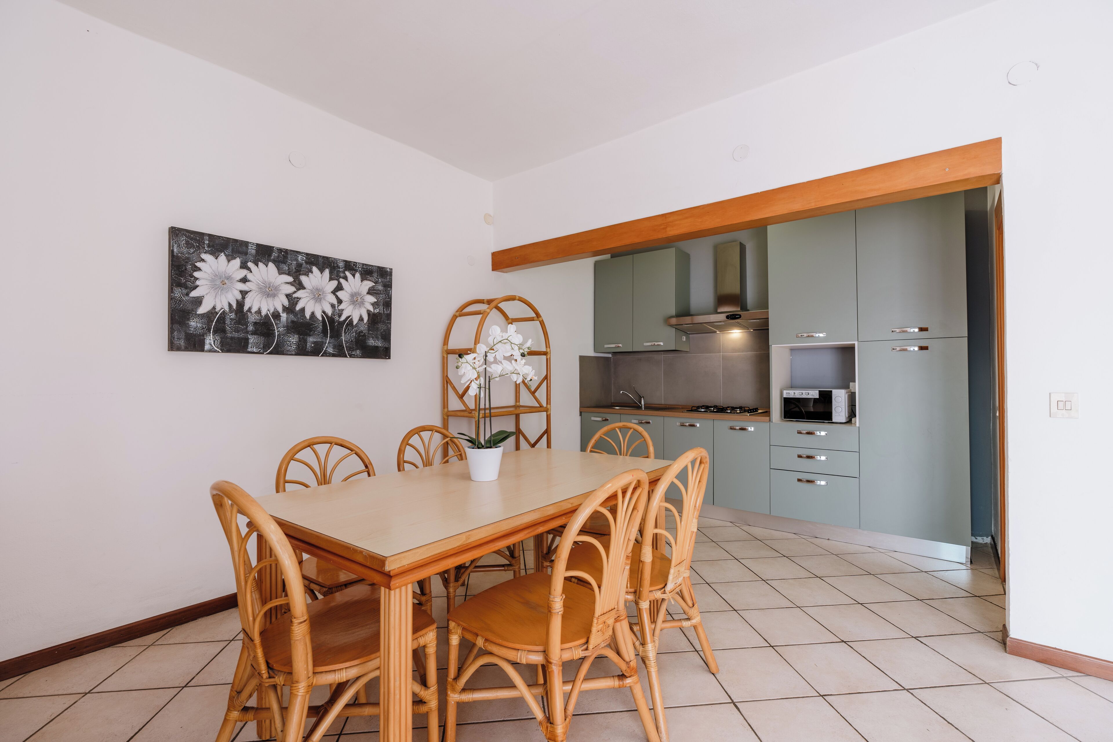 Un comedor con mesa y sillas de madera, una planta en maceta y un cuadro de flores colgado en la pared.