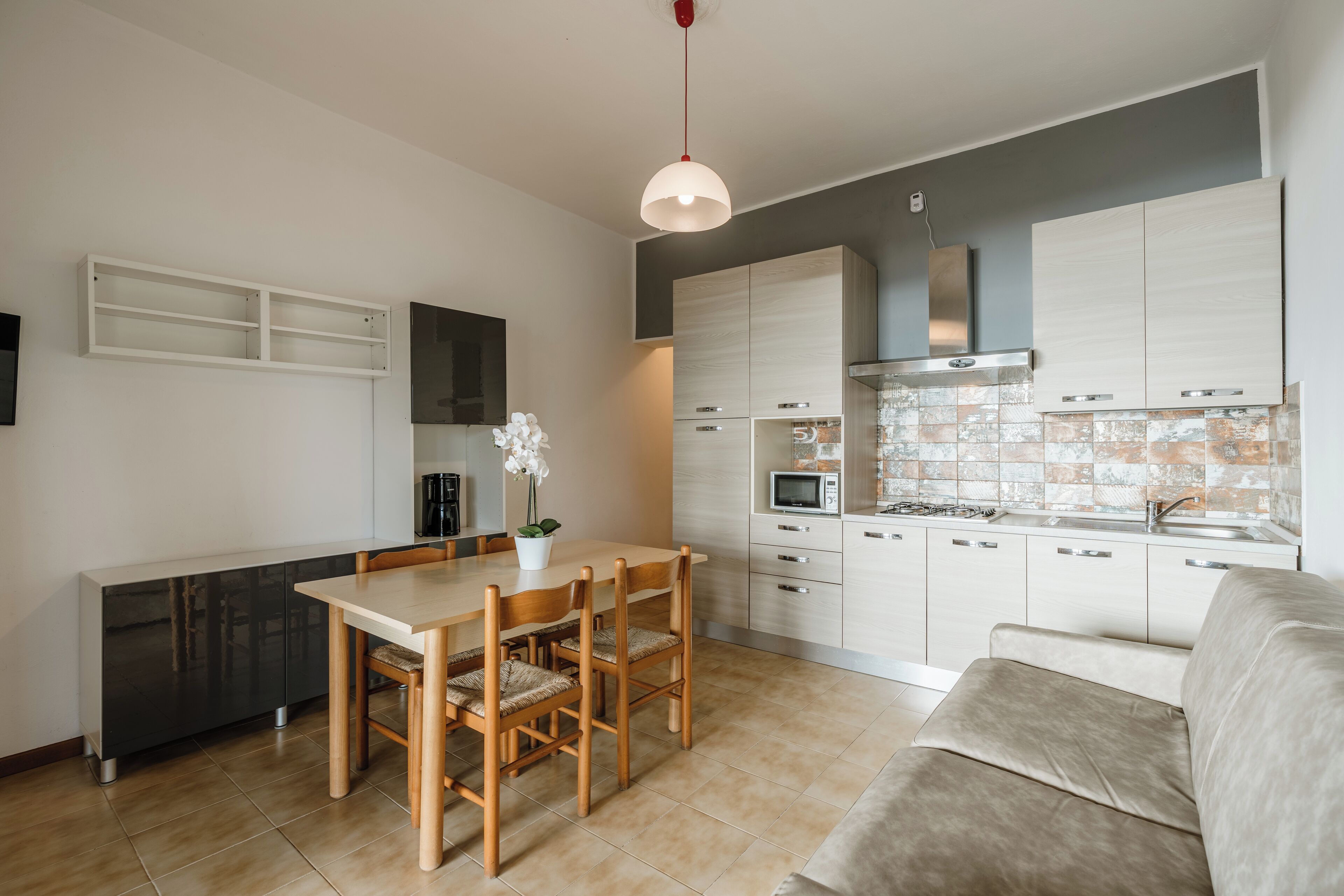 Cozinha moderna com área de refeições, sofá e luminária pendente.