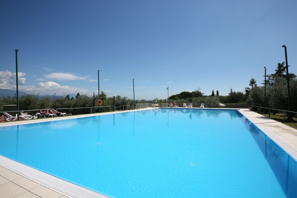 Una piscina rectangular con agua cristalina azul, rodeada por un deck con baldosas y barandales metálicos.